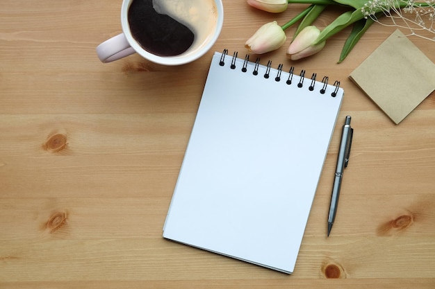 Notebook sticky note coffee cup and pink tulips on wooden background