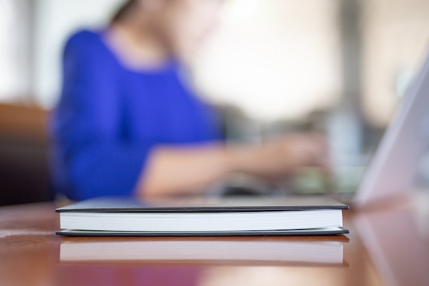 Notebook on the table with woman woking on laptop in blur background.