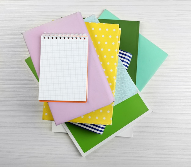 Notebook on top of pile of books and magazines on wooden background