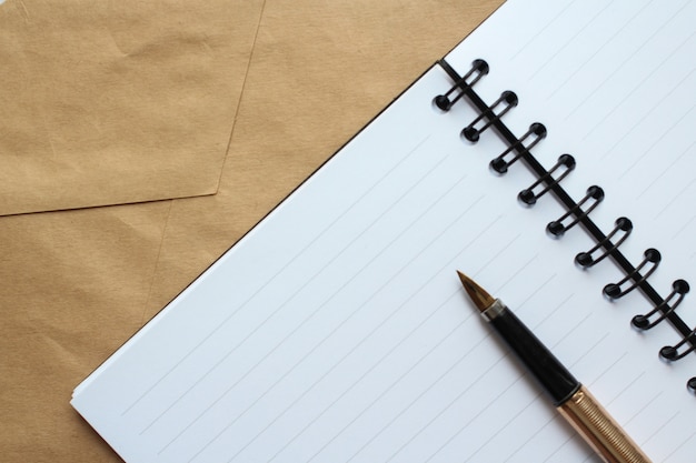 A notebook with clean sheets, an envelope and a gold pen on the table