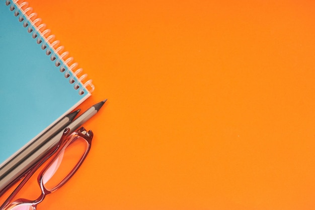 Notebook with eyeglasses and pencils on orange background