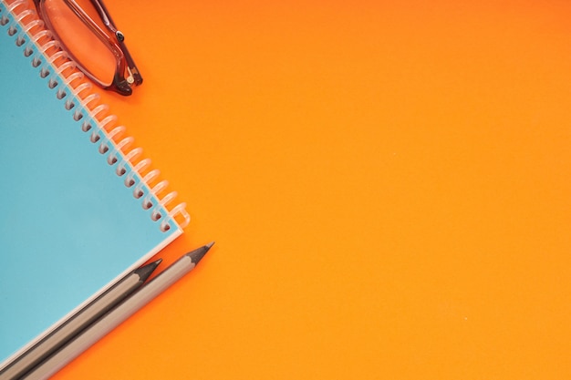 Photo notebook with eyeglasses and pencils on orange background