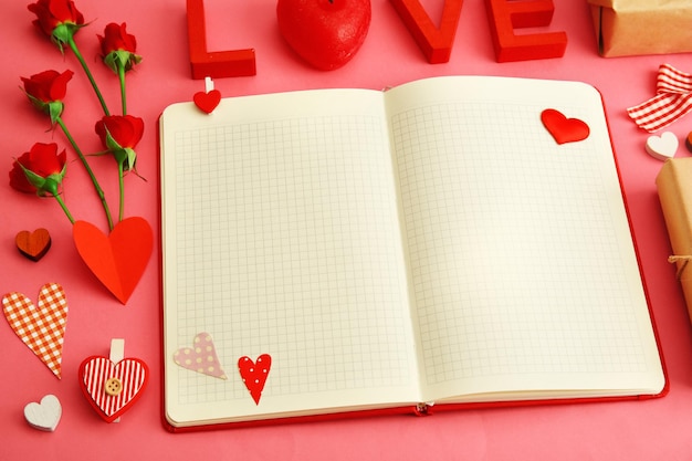 Notebook with gift and Valentine's decor on pink background top view