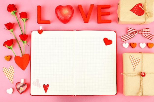 Notebook with gift and Valentine's decor on pink background top view