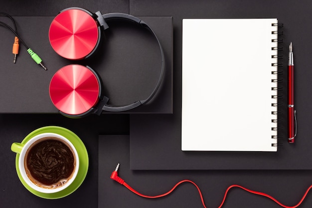 Photo notebook with pen, headphones and cup of coffee at abstract black paper background, minimalism concept style