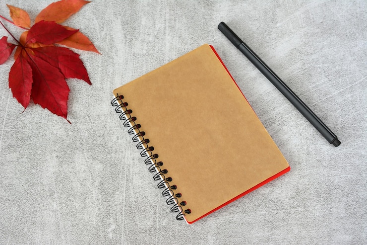 Photo a notebook with a pen on it and a red leaf top view