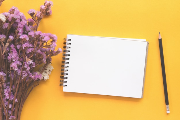 Notebook with pencil and dried flower on yellow background.