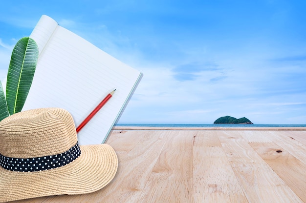 Notebook with pencil and straw hat on wooden floor with sea nature landscape background