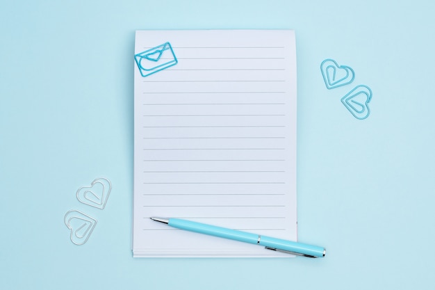 Photo notebook with stationary items on blue background. paperclips in the shape of heart around the notebook.