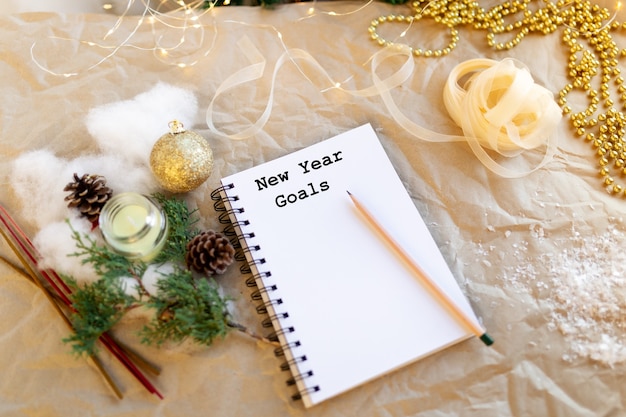 Photo notebook with text new year goals golden christmas decorationnew year lights ribbon fir branch