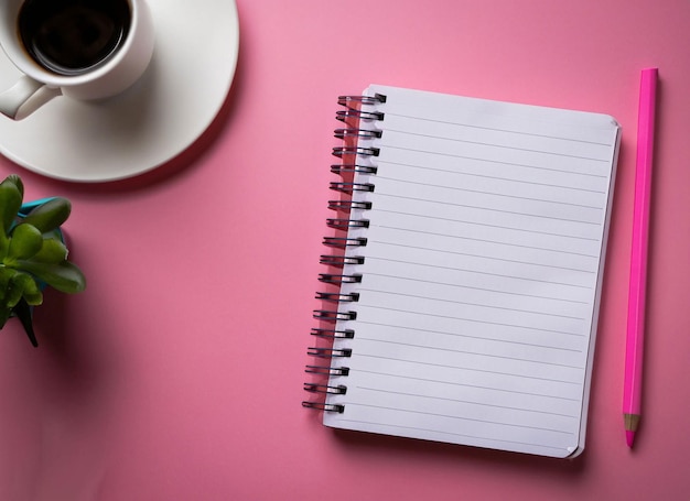 A notebook with the word coffee on it sits on a pink table next to a cup of coffee.