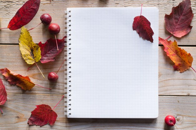 Notebook on wooden autumn  table with dry leaves and red apples