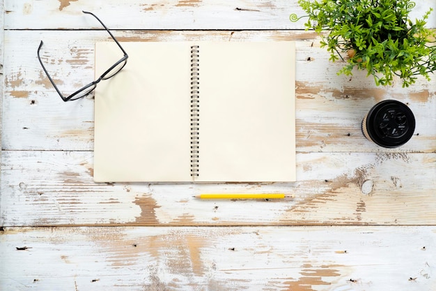 Notebookglazen potloden koffiemokken worden op een wit houten bureau geplaatst