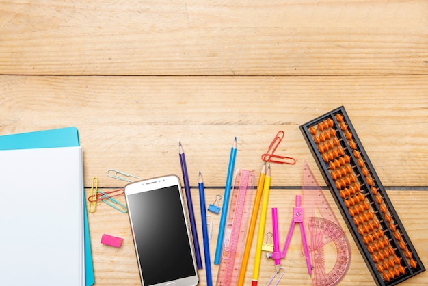 Notebooks en mobiele telefoon met schoolbenodigdheden en briefpapier op de houten tafel