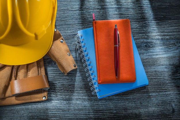 Notebooks pen building helmet tool belt on wooden board.