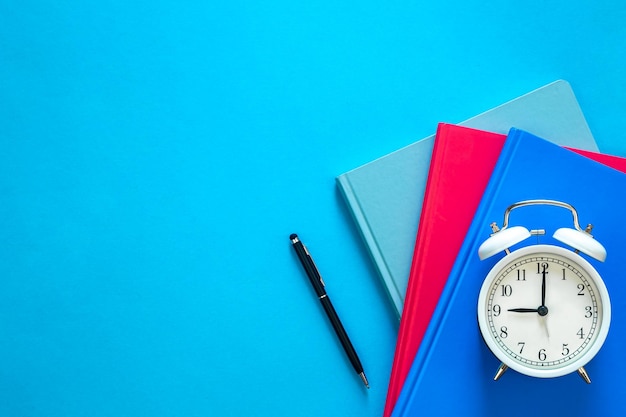 Notebooks pen en wekker op een blauwe achtergrond bovenkant