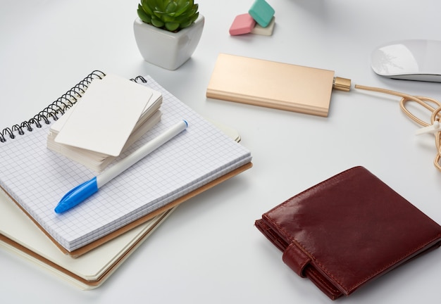 Notebooks, pen, stack of business cards, brown leather wallet and power bank with a cord