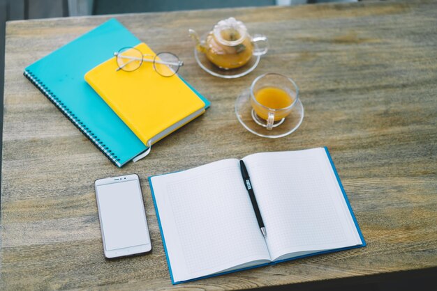 Notebooks and smartphone with glass tea set on desk