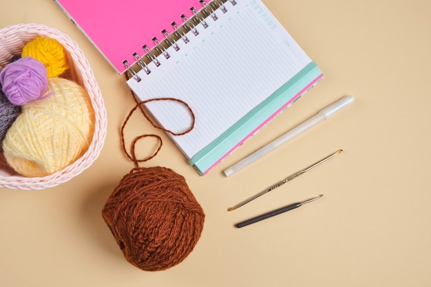 Photo notepad, balls of thread in a basket and crochet hooks on a beige background