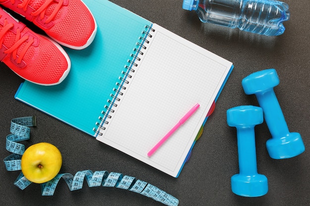 Photo notepad, a bottle of water, an apple, a skipping rope, dumbbells. healthy diet, lifestyle, concept of dumbbells, exercise