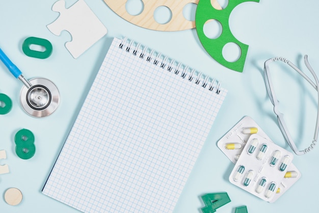 Блокнот, детские очки, стетоскоп, таблетки и игрушки на синем фоне