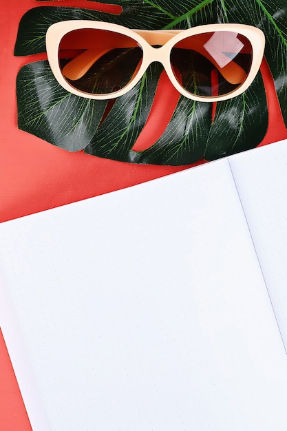 Notepad coral background, sun glasses, hat, money. Top view, copy space. Summer background, travel.