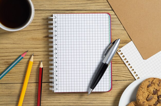 Notepad and cup of coffee with cookies on the table