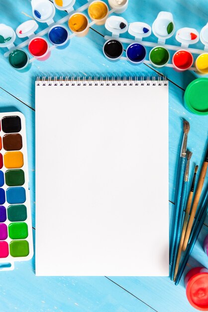 Foto blocco note per disegnare con colori e vernici multicolori su sfondo blu. copia spazio.