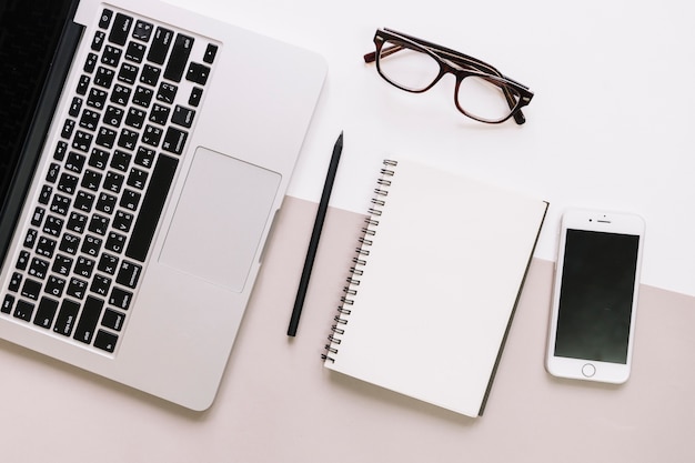 Notepad and glasses between laptop and smartphone