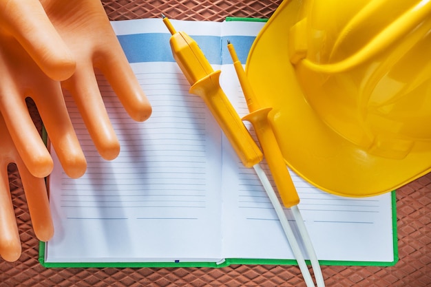 Notepad hard hat insulating gloves electrical tester on dielectric mat.