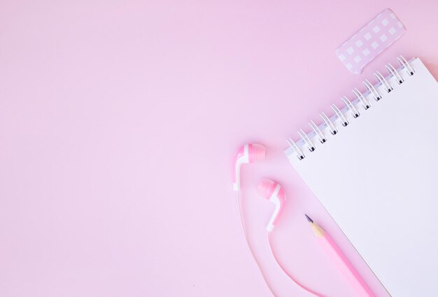 Notepad headphones and pencil on a pink background