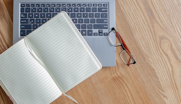 Photo notepad, laptop and glasses on old wooden desk. view from above with copy space in vintage tone