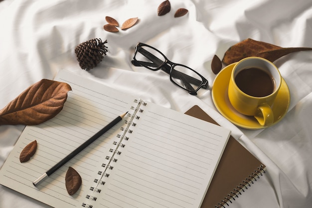 notepad letter cup of coffee and a book with a blanket  on a white textile in bed.