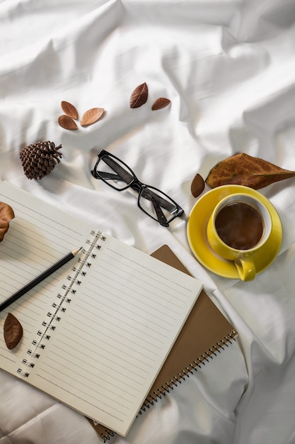 Notepad letter cup of coffee and a book with a blanket  on a white textile in bed.