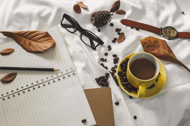 Notepad letter cup of coffee and a book with a blanket  on a white textile in bed.