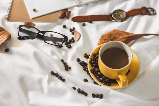 notepad letter cup of coffee and a book with a blanket  on a white textile in bed.
