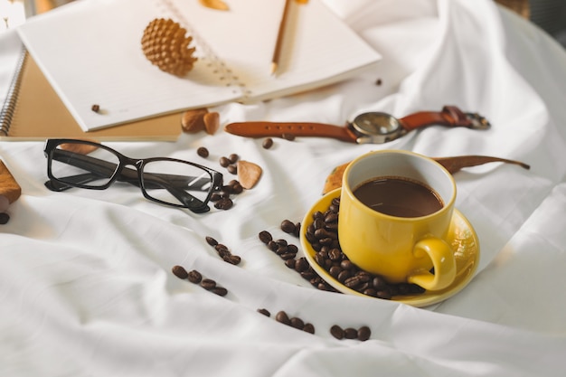 notepad letter cup of coffee and a book with a blanket  on a white textile in bed.