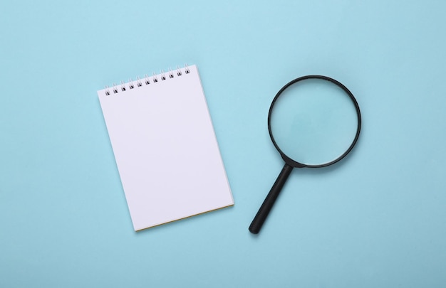 Notepad and magnifier on a blue background top view