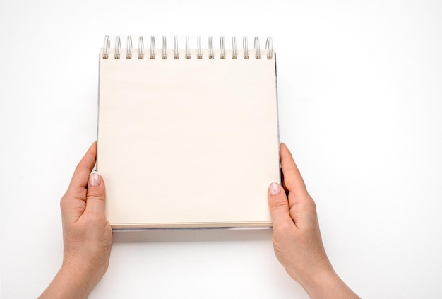 Notepad mockup female hands holding blank spiral notepad or\
calendar over white table background hands shows open notebook\
female hands holding blank white notebook copy space