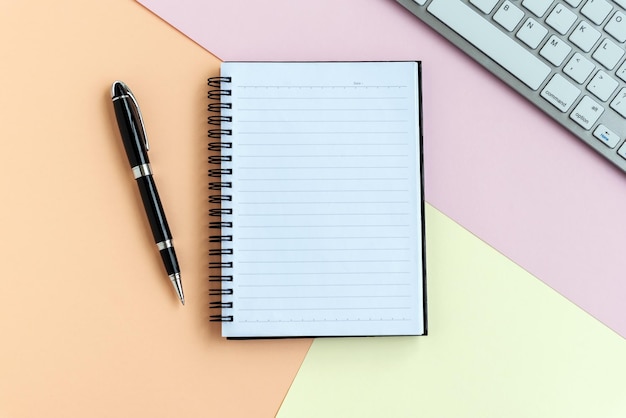 Notepad pen computer keyboard on top of pastel colored background