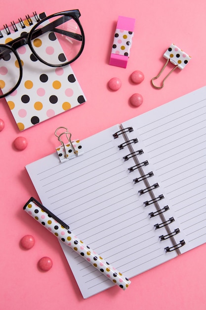 Notepad, pen and glasses on pink background