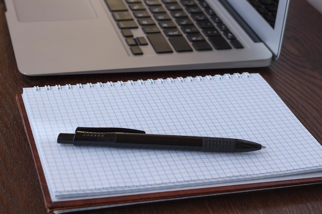 Notepad and pen near laptop on the table