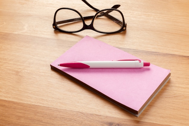 Notepad, pencil and glasses on the wooden background