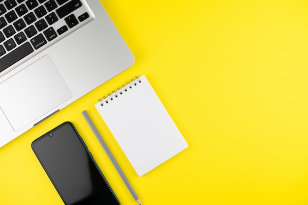 Notepad, pencil, phone and laptop on yellow