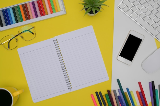 notepad smart phone glasses and smart phone and colored crayons on yellow background