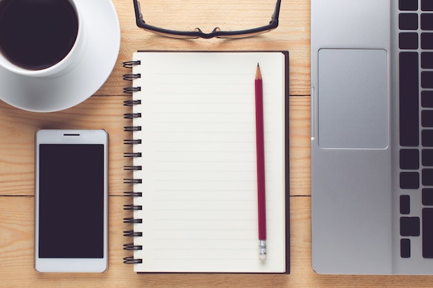 Notepad, smartphone, pen and cup of coffee on wood table