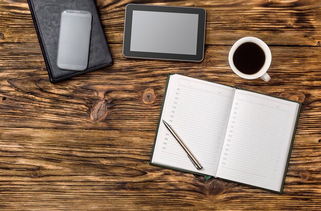 Notepad, tablet PC, smartphone and cup of coffee on the office table. Business and education concept. Top view.