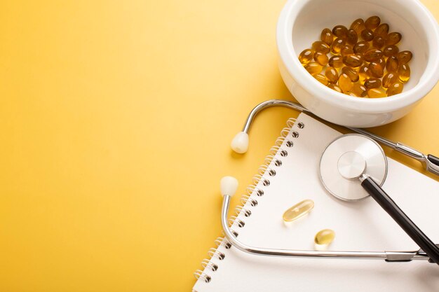 Notepad vitamins pills and stethoscope on a yellow background Place for text