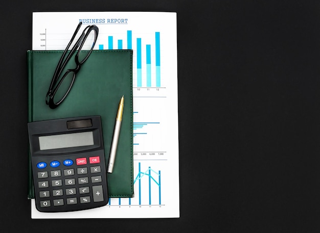 Notepad with business graphs calculator eyeglasses and pen on black Top view Business concept
