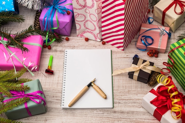 Notepad with pen and colorful gift boxes on wooden table. Celebration and presents